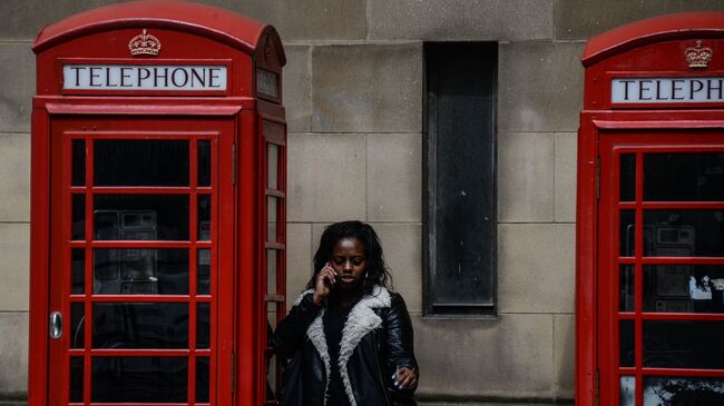 Девушка разговаривает по телефону у телефонной будки. Архивное фото