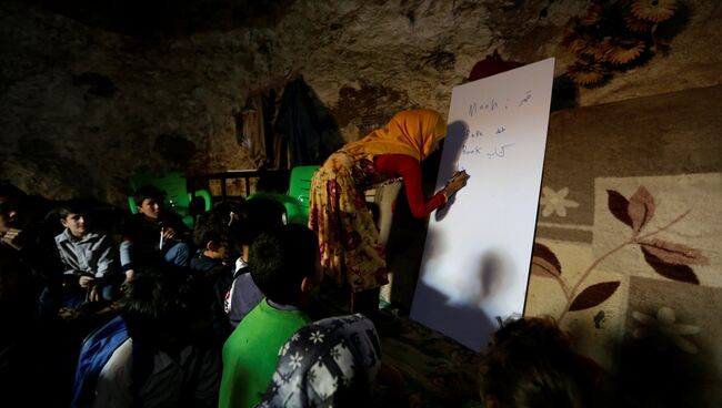 Учитель проводит урок для детей в бомбоубежище деревни Tramla, в провинции Идлиб. Сирия, 27 марта 2016 года Учитель проводит урок для детей в бомбоубежище деревни Tramla, в провинции Идлиб. Сирия, 27 марта 2016 года