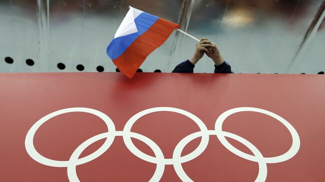 Болельщик держит российский флаг над логотипом олимпийских игр во время зимней Олимпиады-2014 в Сочи