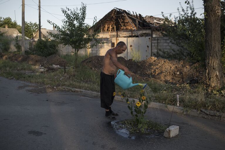 Мужчина поливает цветы на одной из улиц поселка Веселое Донецкой области