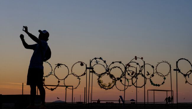 Молодой человек делает селфи на фоне самодельных олимпийских колец на пляже Копакабана