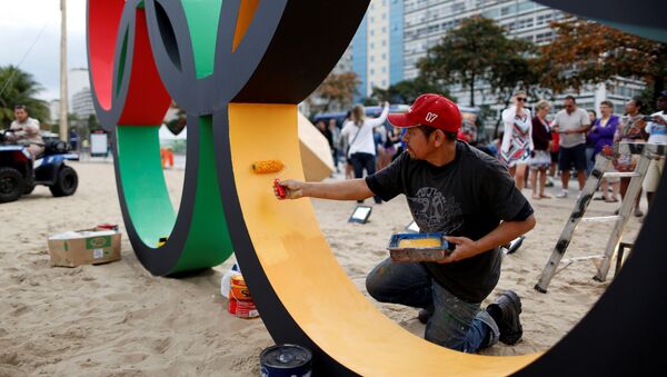 Работник красит олимпийские кольца на пляже Копакабана в Рио-де-Жанейро, Бразилия