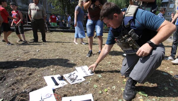 Представитель Специальной мониторинговой миссии ОБСЕ осматривают воронку от снаряда во время фиксации разрушений в Ясиноватой