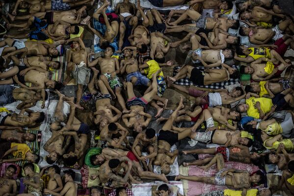 Заключенные спят на земле, на открытой баскетбольной площадке в филиппинской тюрьме.