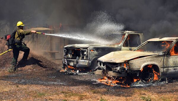 Пожарный тушит автомобили, загоревшиеся в результате лесных пожаров в Калифорнии. 14 августа 2016