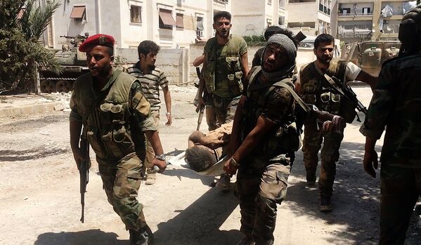 Бойцы сирийской армии выносят раненого при штурме военных училищ на юго-западе Алеппо