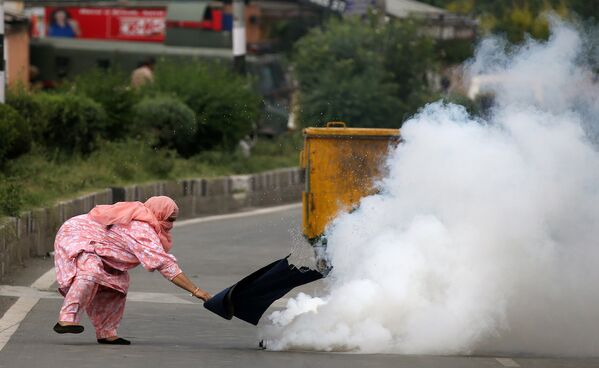 Женщина пытается потушить горящую канистру со слезоточивым газом во время протестов в Кашмире, Индия