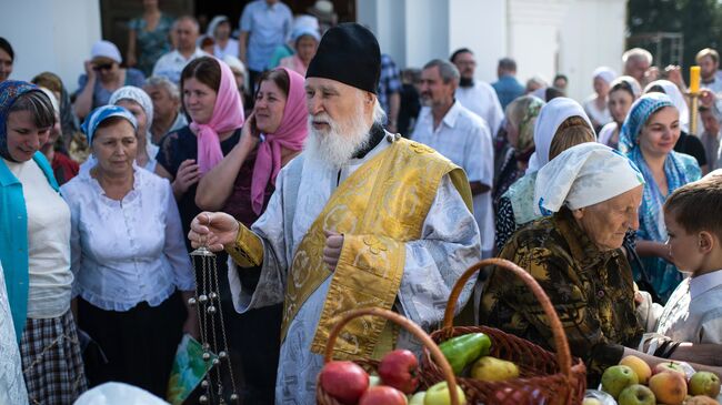 Священнослужитель и верующие во время богослужения в честь праздника Преображения Господня у собора Воздвижения Креста Господня в Омске