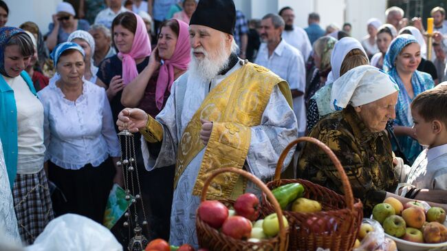 Священнослужитель и верующие во время богослужения в честь праздника Преображения Господня у собора Воздвижения Креста Господня в Омске