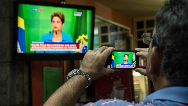 Мужчина записывает выступление по бразильскому телевидению временно отстраненной от должности Дилмы Роуссефф. Архивное фото