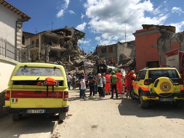 Люди у разрушенных в результате землетрясения домов в городе Аматриче