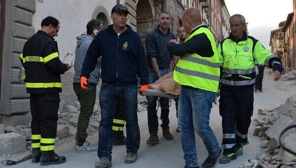 Сотрудники спасательных служб несут на носилках человека, спасенного из-под завалов, в городе Аматриче,