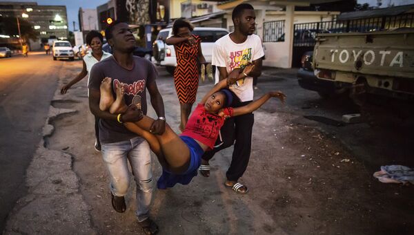Люди несут в госпиталь девушку, потерявшую сознание в ходе столкновений с полицией после результатов президентских выборов в Габоне. Август 2016