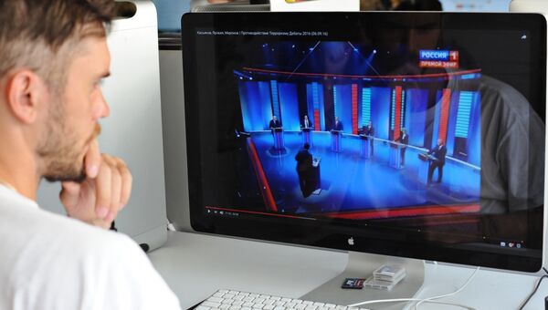 Молодой человек смотрит предвыборные теледебаты с экрана монитора. Архивное фото