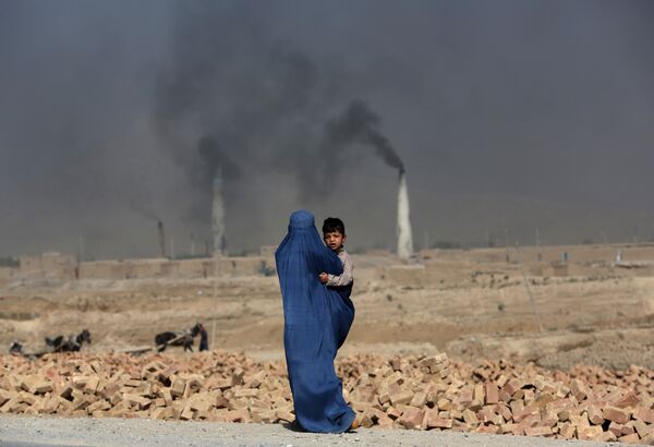 Женщина с ребенком на руках идет мимо кирпичного завода на окраине Кабула, Афганистан
