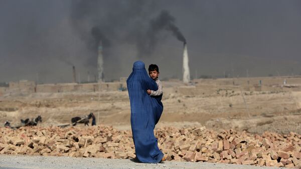 Женщина с ребенком на руках идет мимо кирпичного завода на окраине Кабула, Афганистан. Архивное фото