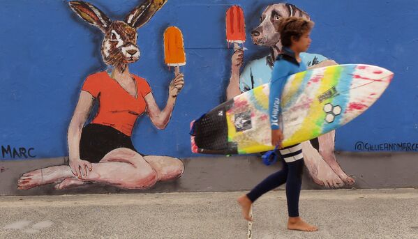 Серфер идет вдоль стены с граффити в Сиднее