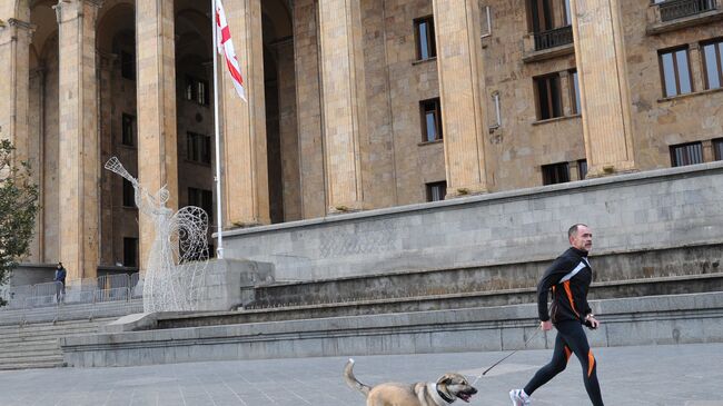 Мужчина с собакой на пробежке перед зданием парламента в Тбилиси