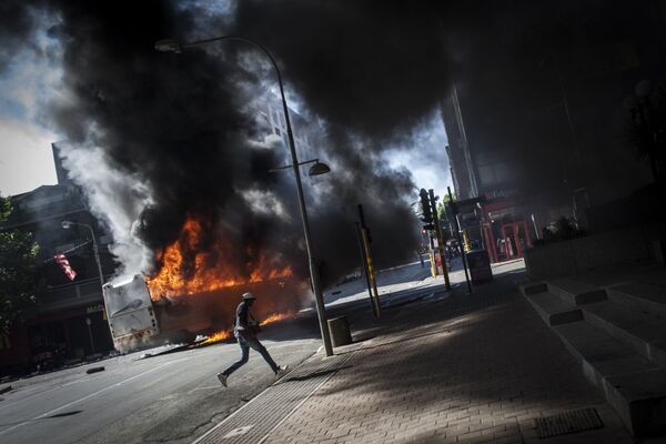Протестующий идет мимо подожженного автобуса, во время студенческой акции протеста в Йоханнесбурге, Южная Африка