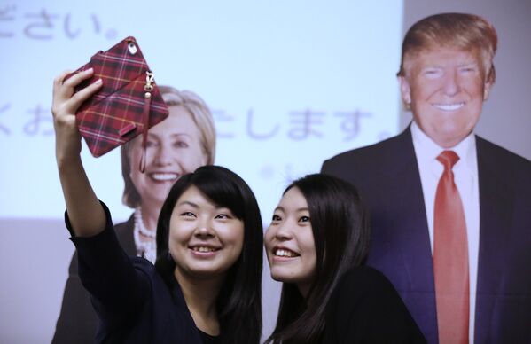 Студентки фотографируются на фоне изображений Дональда Трампа и Хиллари Клинтон в посольстве США в Токио