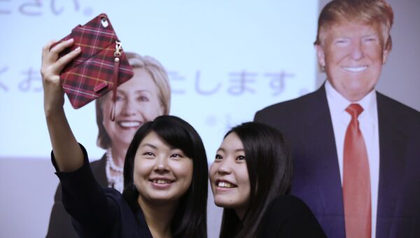 Студентки фотографируются на фоне изображений Дональда Трампа и Хиллари Клинтон в посольстве США в Токио