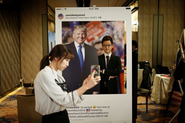 Девушка фотографирует своего друга на фоне портрета кандидата в президенты США Дональда Трампа в отеле в Сеуле