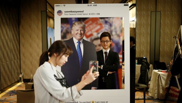 Девушка фотографирует своего друга на фоне портрета кандидата в президенты США Дональда Трампа в отеле в Сеуле