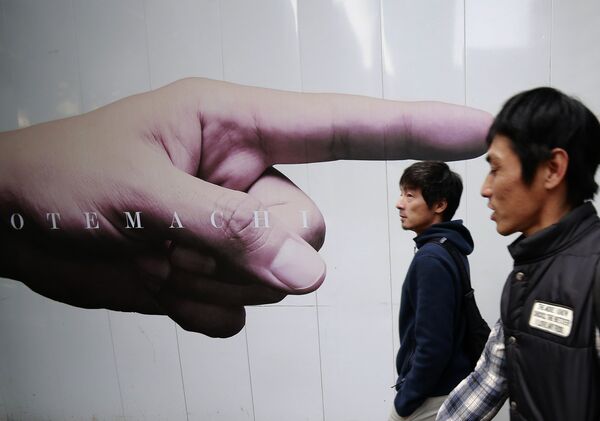 Мужчины проходят рекламные объявления, размещенные на заборе строительной площадки в Токио, Япония. 7 ноября 2016