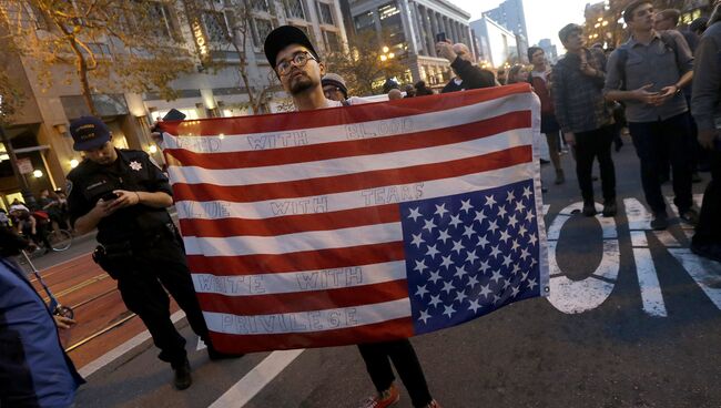 Участник акции протеста против избранного президента США Дональда Трампа с перевернутым флагом США в Сан-Франциско
