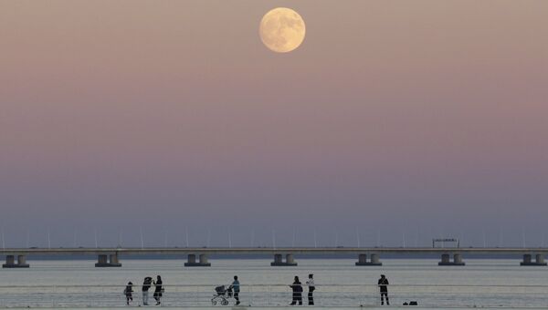 Люди прогуливаются вдоль реки Тежу на фоне луны в Лиссабоне, Португалия. 13 ноября 2016