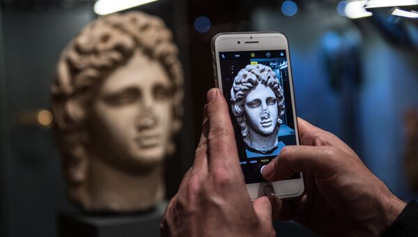 Посетитель фотографирует на мобильный телефон скульптурное изображение Александра Великого на открытии выставки Боги и герои Древней Греции