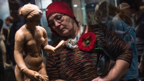 Посетительница рассматривает терракотовую статуэтку Афродиты с зеркалом на открытии выставки Боги и герои Древней Греции
