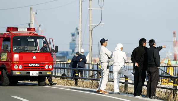 Пожарные и местные жители смотрят на море после предупреждения о возможном цунами в городе Сома, Япония