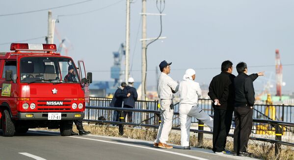 Пожарные и местные жители смотрят на море после предупреждения о возможном цунами в городе Сома, Япония