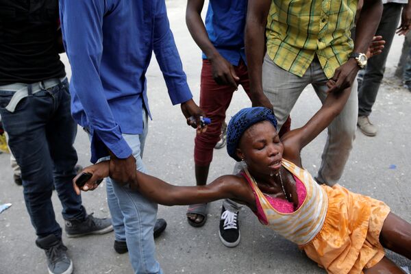 Люди помогают женщине, пострадавшей от слезоточивого газа во время демонстраций в Порт-о-Пренсе, Гаити