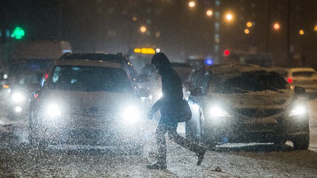 Прохожий переходит дорогу в Москве во время снегопада