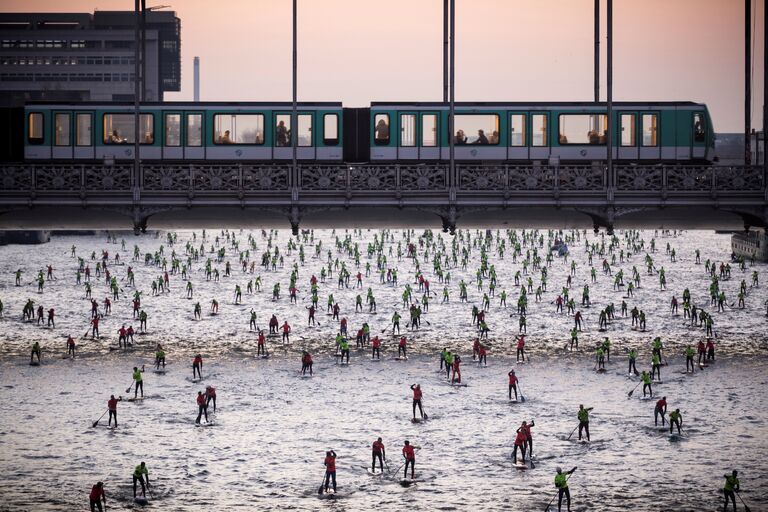 Люди принимают участие в 7-ом ежегодном Nautic SUP Paris Crossing на реке Сена в Париже, Франция