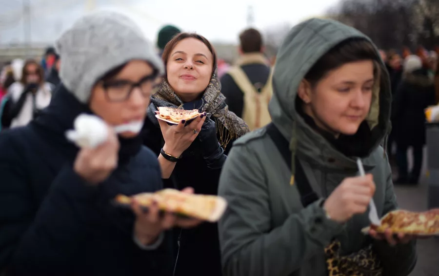 Девушки едят блины во время масленичных гуляний в Парке Горького в Москве Девушки едят блины во время масленичных гуляний в Парке Горького в Москве