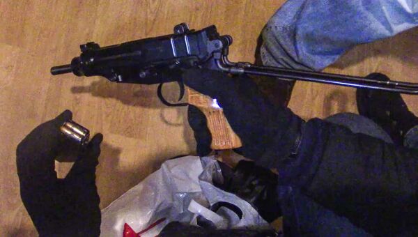 Сотрудник правоохранительных органов демонстрирует огнестрельное оружие и магазин с патронами к нему, изъятое сотрудниками ФСБ РФ у задержанной в Москве диверсионно-террористической группы
