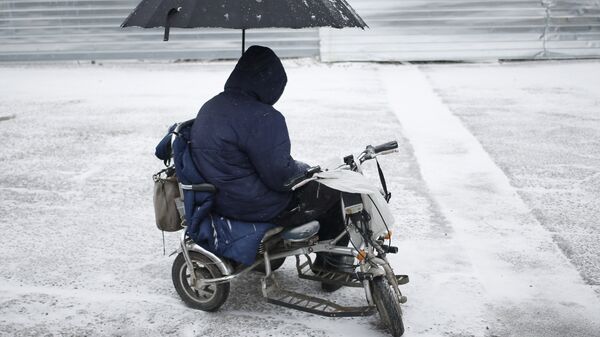 Мужчина в инвалидной коляске, под зонтом, на одной из улиц Симферополя