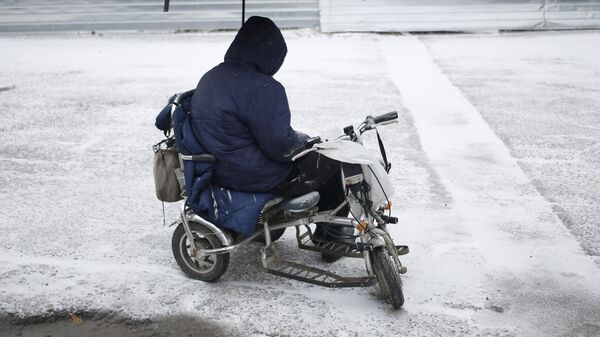 Мужчина в инвалидной коляске, под зонтом, на одной из улиц Симферополя