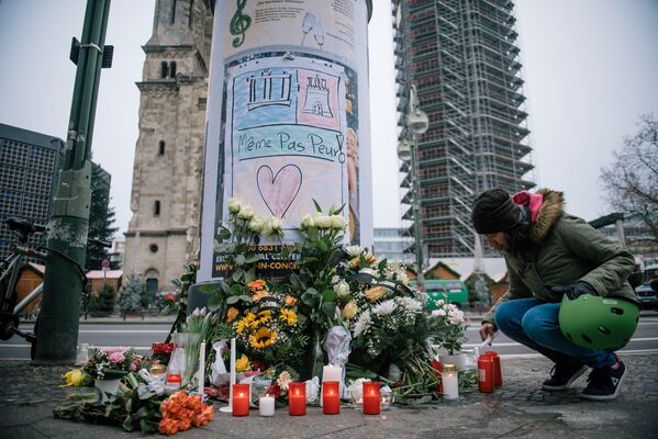 Девушка зажигает свечу недалеко от места теракта в Берлине