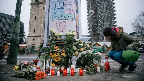 Девушка зажигает свечу недалеко от места теракта в Берлине