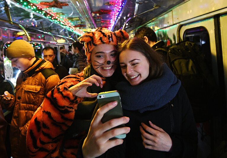 Пассажиры фотографируются в новогоднем поезде Московского метро, украшенном гирляндами и еловыми ветками