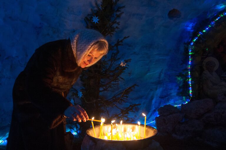 Женщина зажигает свечу в снежном Рождественском вертепе во время праздничной Рождественской службы в Богоявленском соборе в Томске