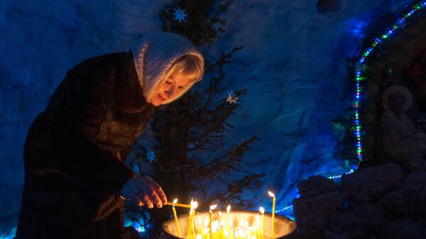 Женщина зажигает свечу в снежном Рождественском вертепе во время праздничной Рождественской службы в Богоявленском соборе в Томске