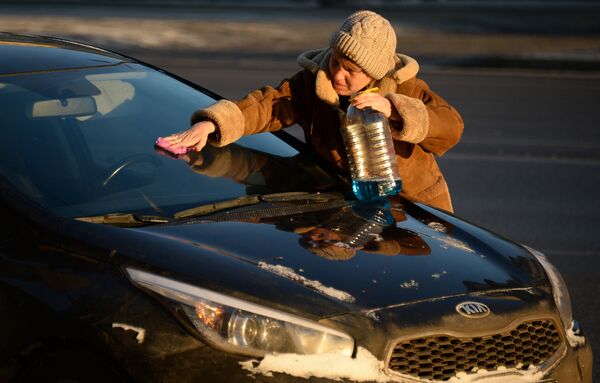 Женщина чистит от инея лобовое стекло машины в морозный день в Москве