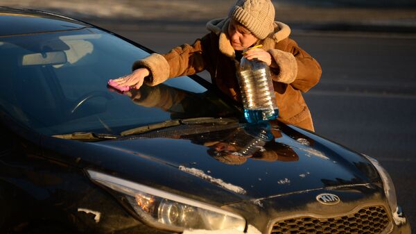 Женщина чистит от инея лобовое стекло машины в морозный день в Москве