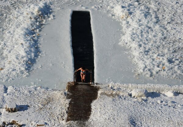 Женщина выходит из проруби на берегу Амурского залива