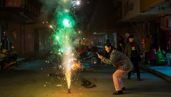 Женщина фотографирует фейерверк в канун китайского Нового года в городе Ляньюньган, провинция Цзянсу, Китай. 27 января 2017